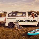 ein Bus an einem See mit offener Hecklappe und de Schriftzug Scan mich Baby &copy;mikar-carsharing