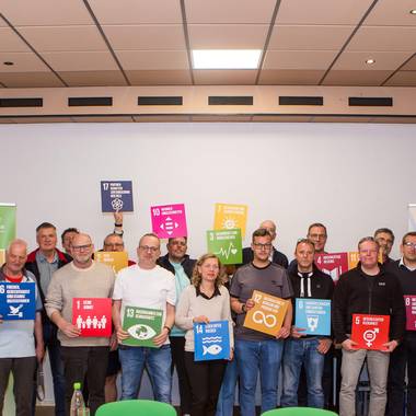 Die Workshopteilnehmer haben sich für ein gemeinsames Foto aufgestellt und zeigen die Tafeln mit den 17 Zielen für eine global nachhaltige Kommune (SDG´s)