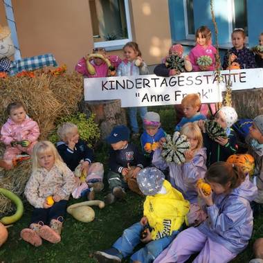 Ein Gruppenbild der KITA Kinder der Anne Frank mit verschiedenen Kürbissen und einer Strohfigur im Hintergrund
