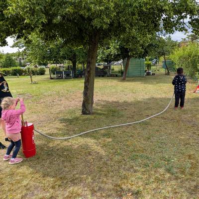 Zu sehen sind zwei Kinder mit Ihrer Erzieherin an einer Feuerlöschpumpe