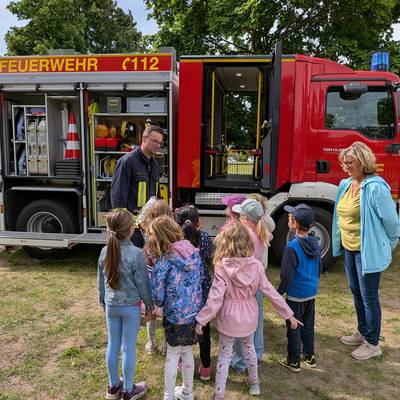 Kinder vor einem Feuerwehrauto die den Ausführungen des Feuerwehrmannes aufmerksam lauschen.